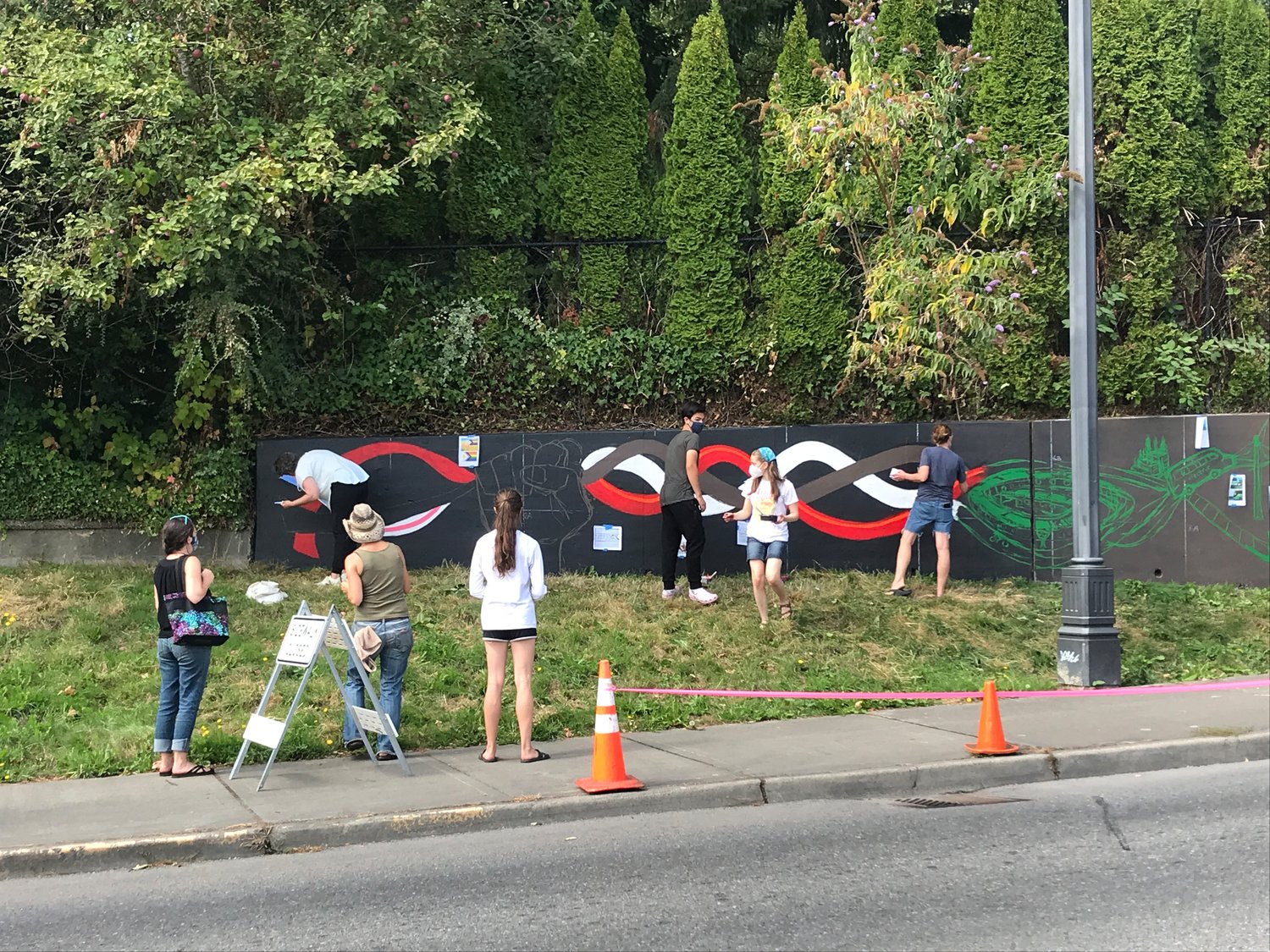 Volunteer artists in October 2021 adorn the retaining wall on Olympic Way in west Olympia with several symbols that make up the Climate Justice Wall there.