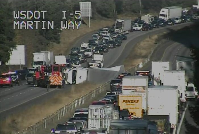 A photo taken by an I-5 traffic camera showing the semi upturned and disrupting traffic.